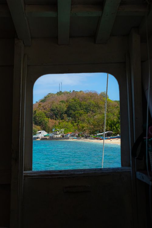 Free Picturesque view of an island and beach from a boat window, featuring clear blue water. Stock Photo