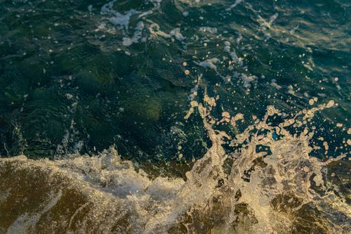 Free Dramatic close-up of an ocean wave crashing with splashing water at sunset. Stock Photo