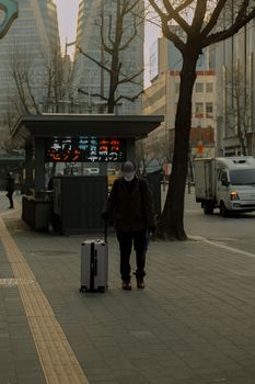 A person walks on an urban sidewalk with a suitcase, surrounded by tall buildings.