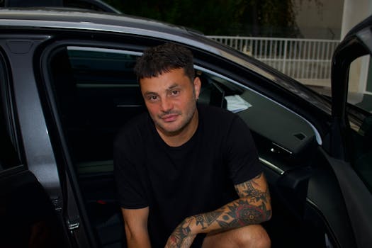 Man with tattoos sitting casually in a car in Maniago, Italy.