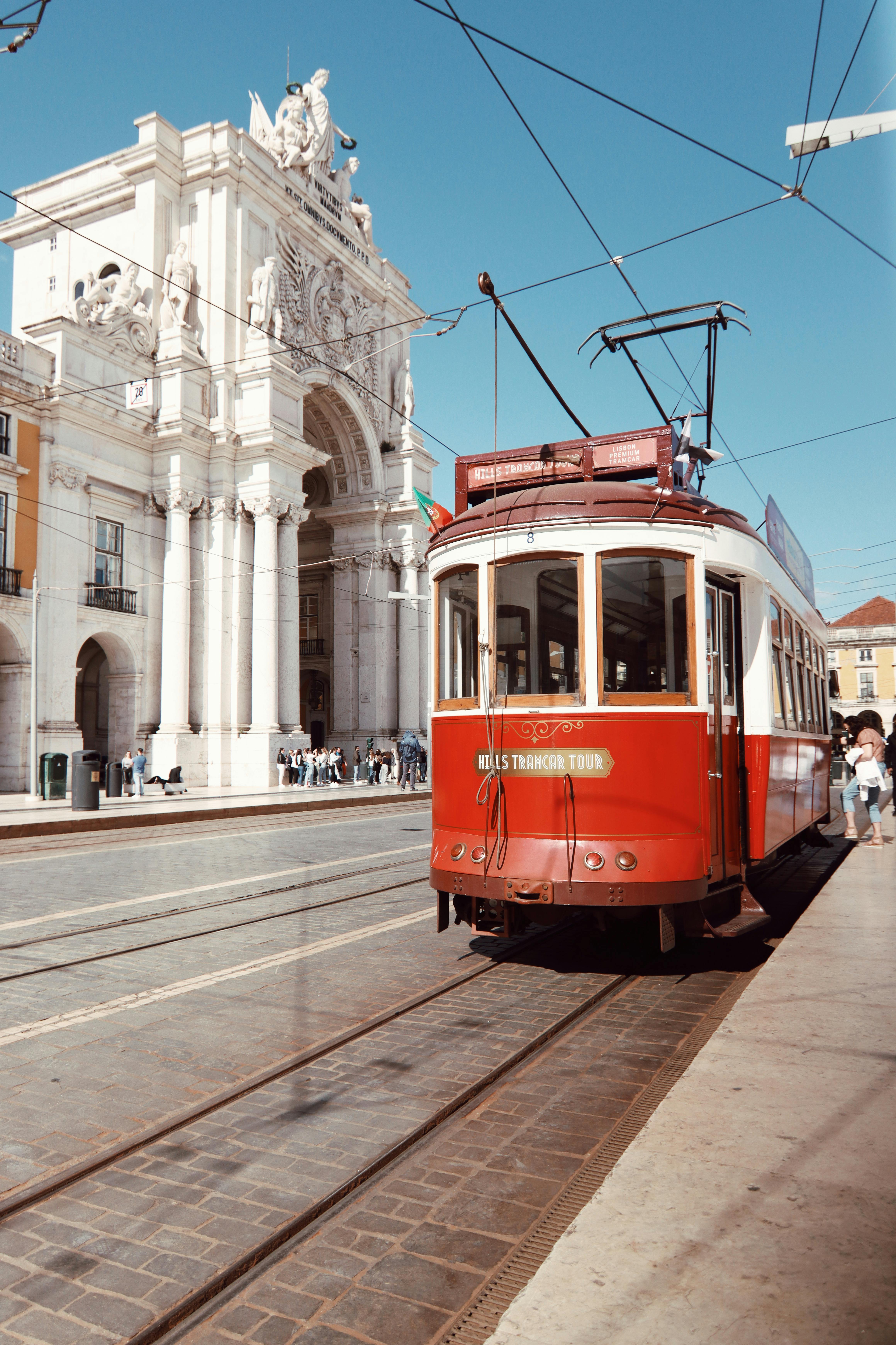 Vintage red tram passing by Arco da Rua Augusta, a famous landmark in Lisbon, Portugal.