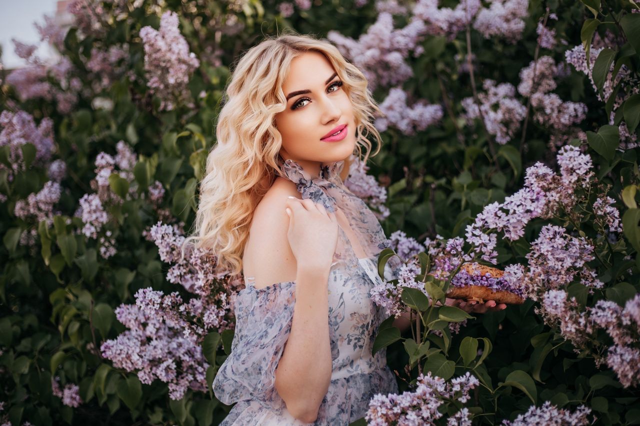 stylish blonde woman in a sundress surrounded by lilac flowers perfect