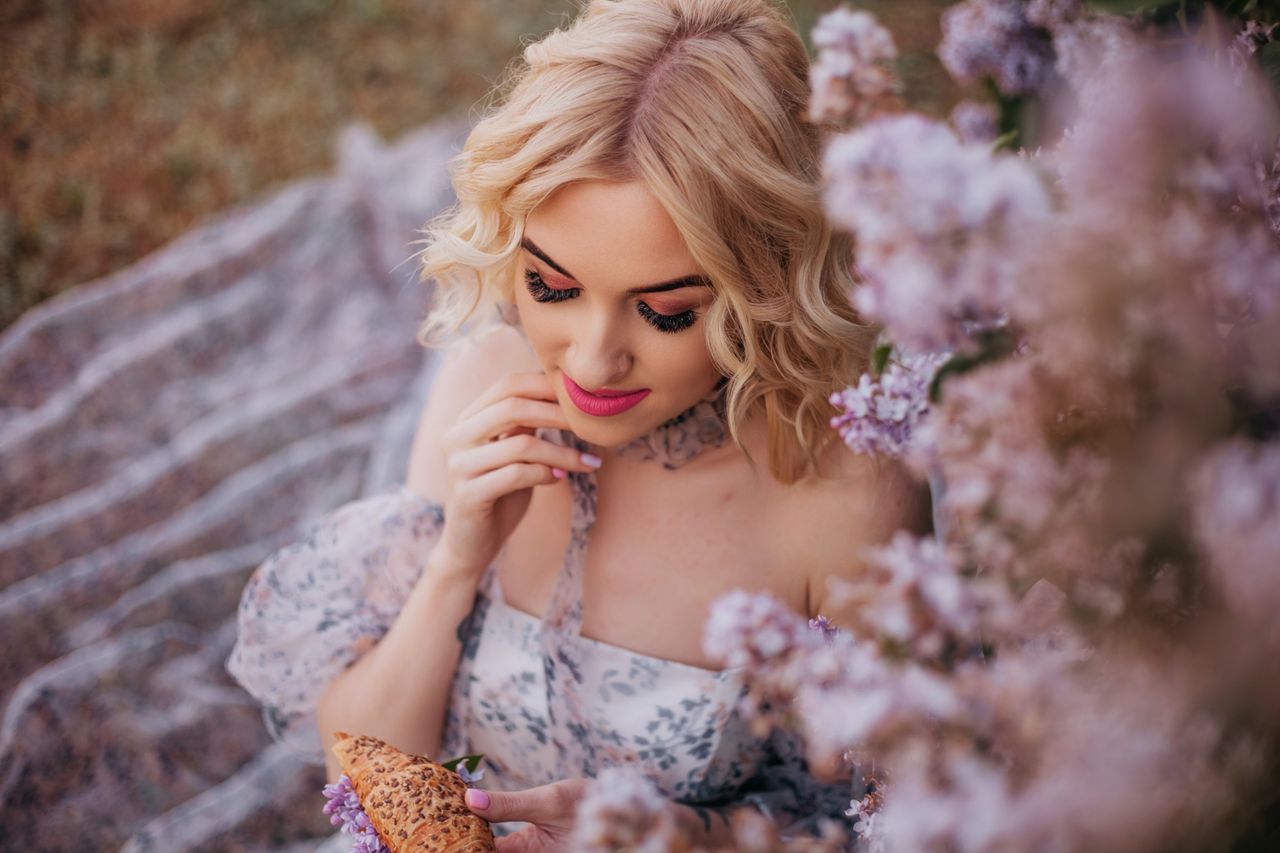 stylish woman with blonde hair holds a croissant in a spring floral se
