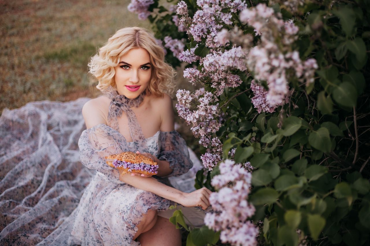 a stylish woman in a floral dress poses elegantly next to blooming lil