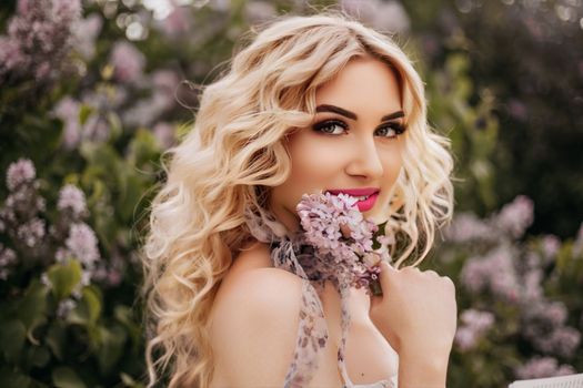 Captivating outdoor portrait of a smiling blonde woman holding lilac flowers, embodying spring beauty.
