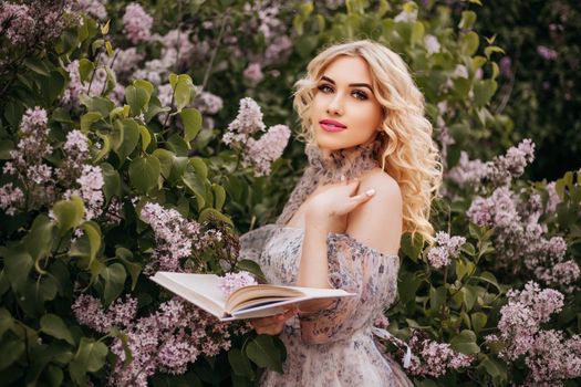 A beautiful woman stands with a book among blooming lilacs, capturing spring elegance and natural beauty.