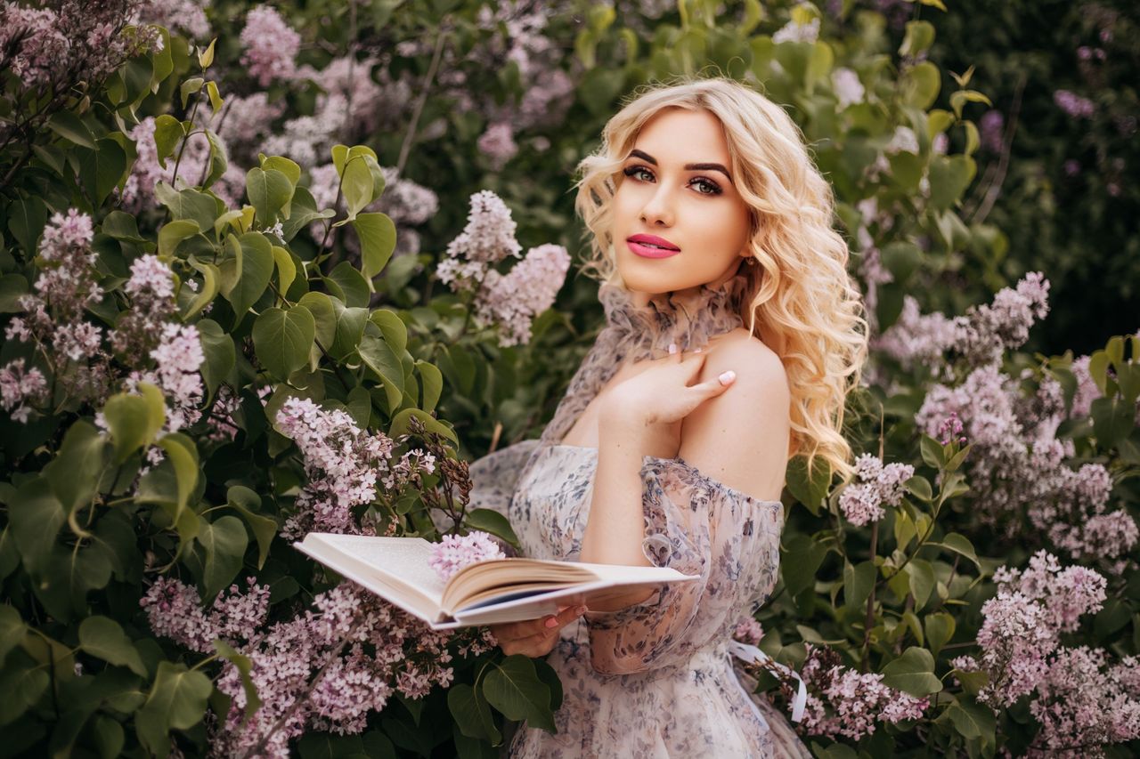 a beautiful woman stands with a book among blooming lilacs capturing s