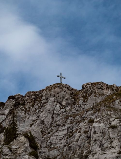 Free A distant view of a cross atop a rocky cliff under the blue sky in Greyerz, Switzerland. Stock Photo