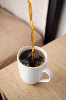 A steaming cup of coffee being poured into a white mug on a wooden table.