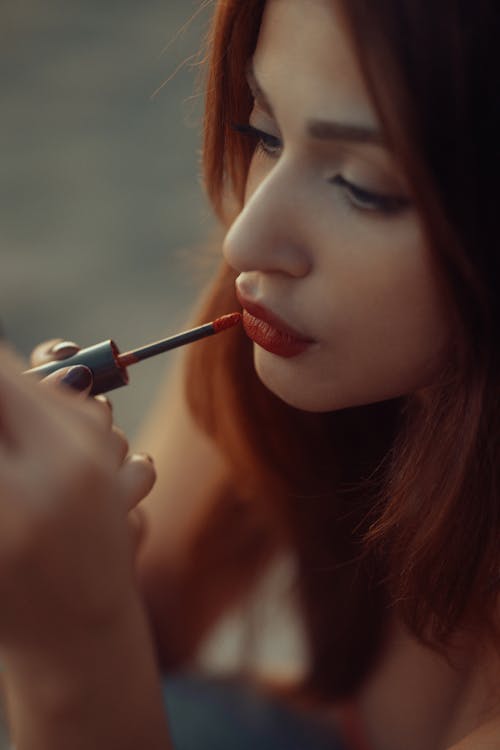A woman with red hair is applying lipstick