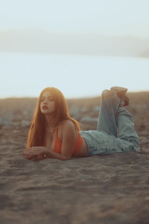 Free Stylish woman in casual jeans and top poses on beach during sunset. Stock Photo
