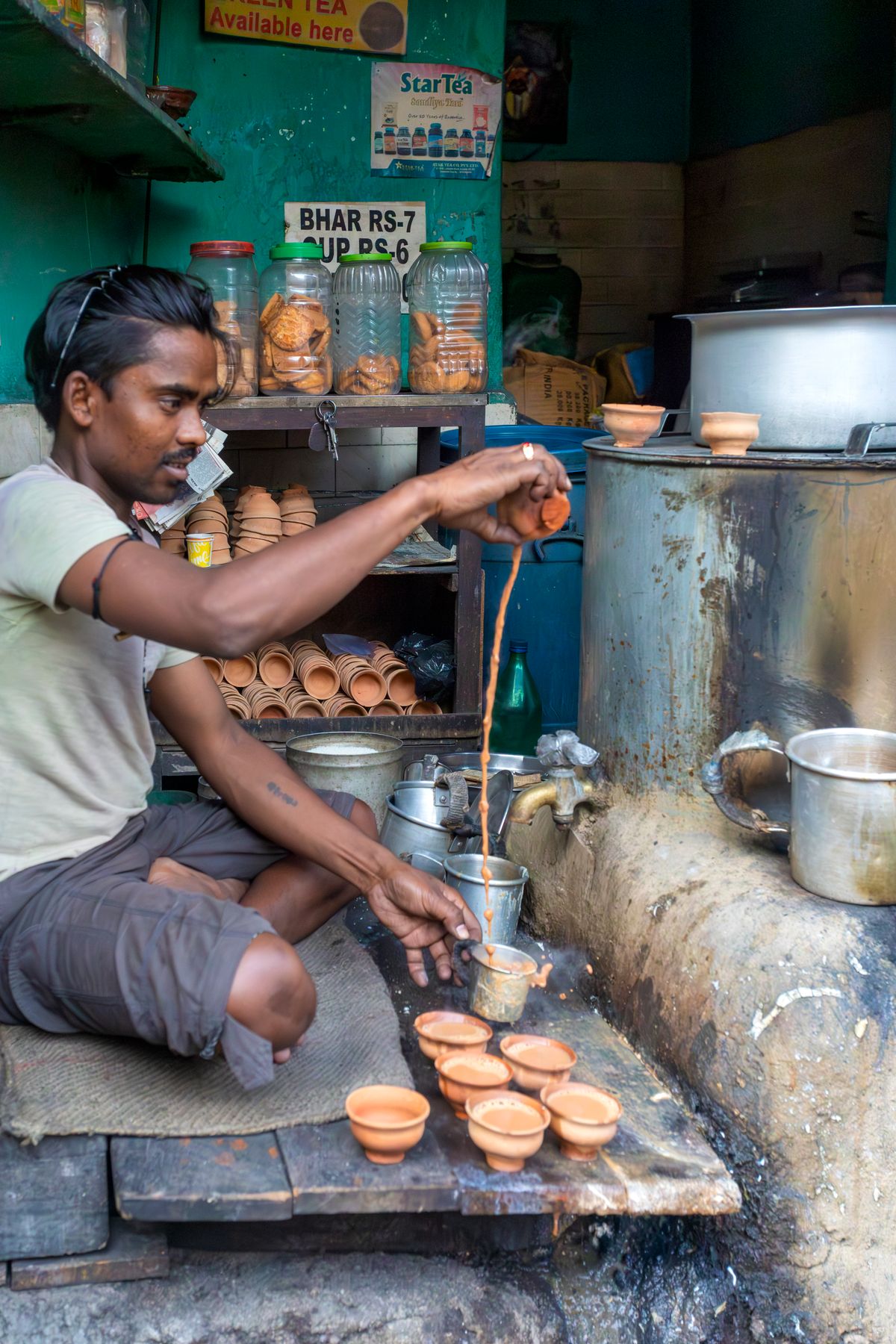 A vendor pouring masala chai into clay cups at an Indian street stall