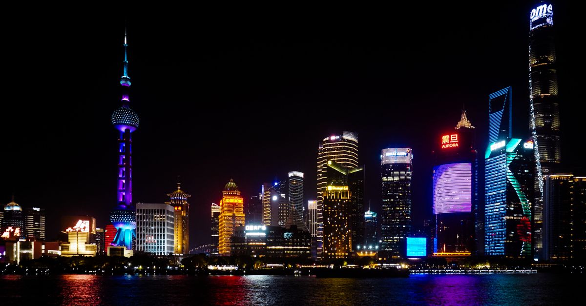 Vibrant Shanghai skyline at night featuring iconic skyscrapers and colorful lighting reflections on water.