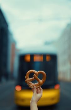 A hand holding a pretzel with a blurred tram in the background in Berlin.