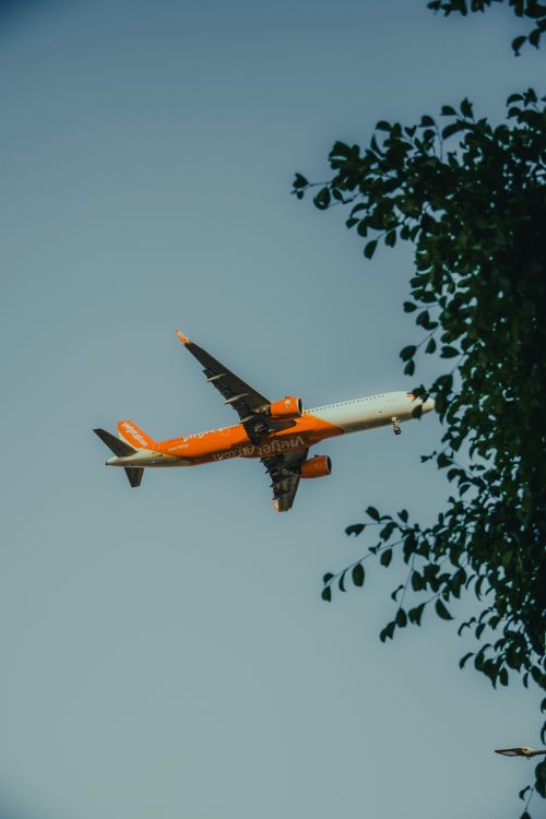 Free Orange and white commercial airplane flying beneath a clear blue sky. Stock Photo