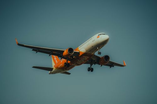 Free A vibrant orange airplane soaring through a clear sky, captured from below. Stock Photo
