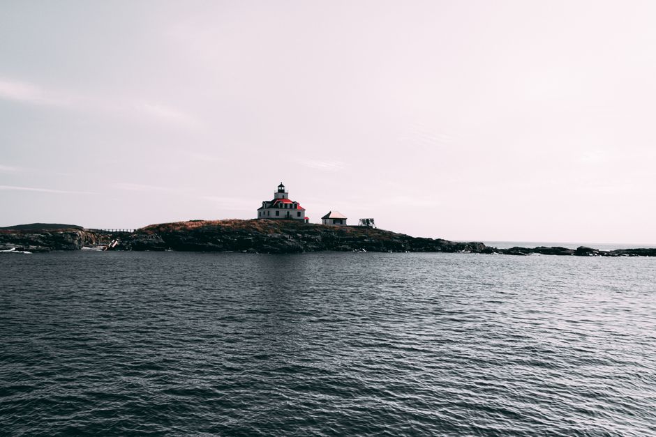 A picturesque lighthouse on a rocky island during dusk against a tranquil sea.