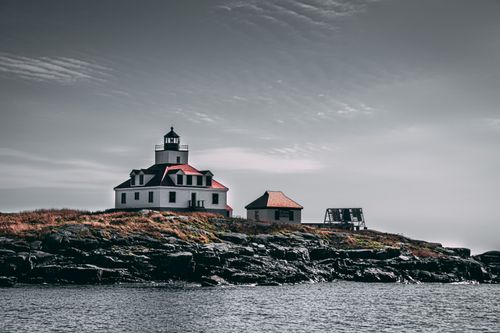 Free A picturesque lighthouse stands on a rocky island under a clear sky. Stock Photo