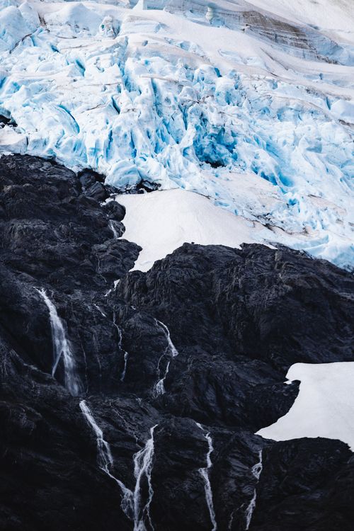 Free Stunning aerial view of a frozen glacier contrasting with rugged dark rocks, capturing nature's raw beauty. Stock Photo