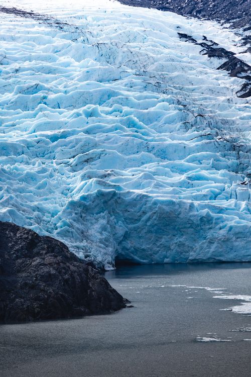 Free Stunning view of a glacier descending into icy water, showcasing rugged mountainous terrain. Stock Photo