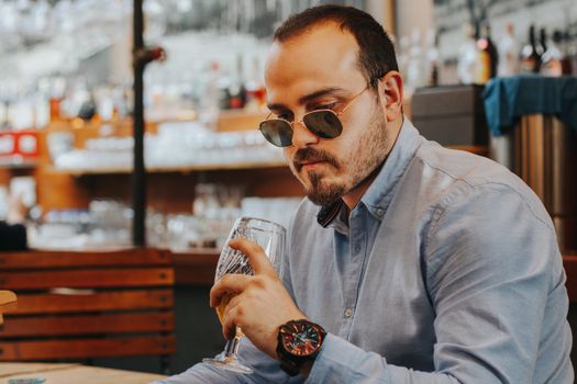 A fashionable man with sunglasses and wristwatch savoring a drink in a chic Istanbul café.