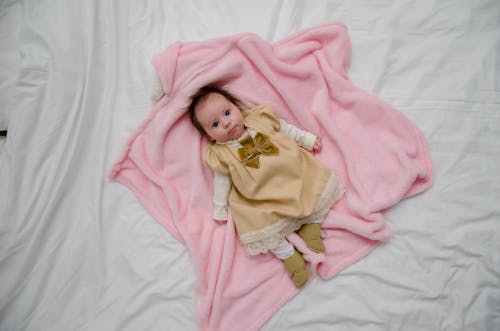 Bebé En Vestido Blanco Y Amarillo Sobre Textil Rosa