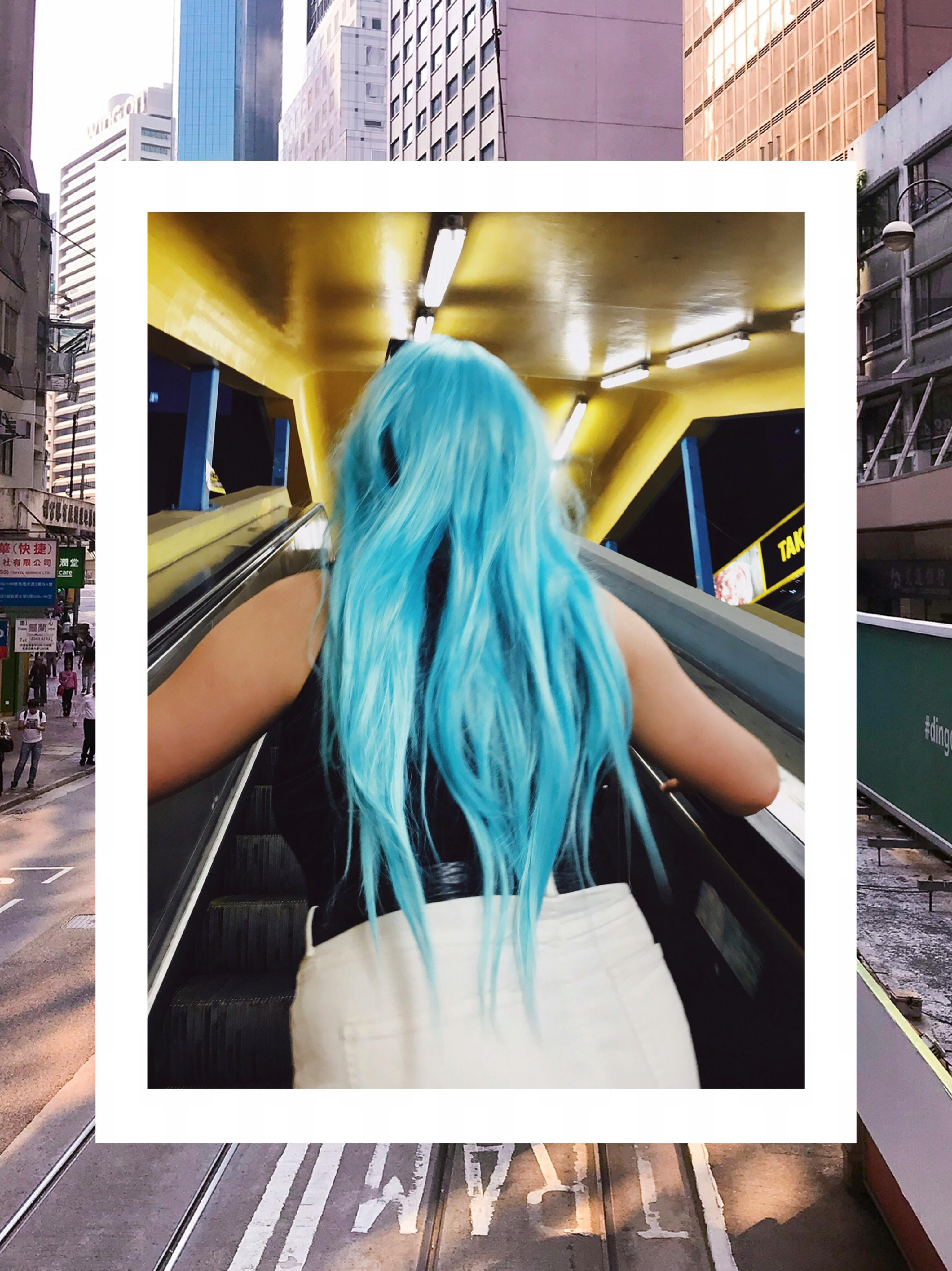 在现代城市环境中，一位蓝发女子乘坐着室内自动扶梯