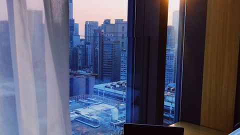 Cozy hotel room in Kowloon, Hong Kong overlooking the city skyline at dawn.