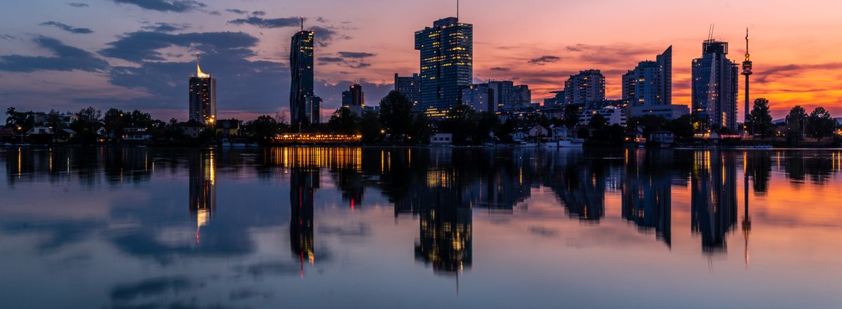 Tranquil reflection of Vienna's cityscape at sunset, showcasing serene waters and vibrant skies.