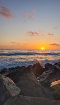 A beautiful sunset over a rocky shoreline, capturing waves and vibrant sky colors.