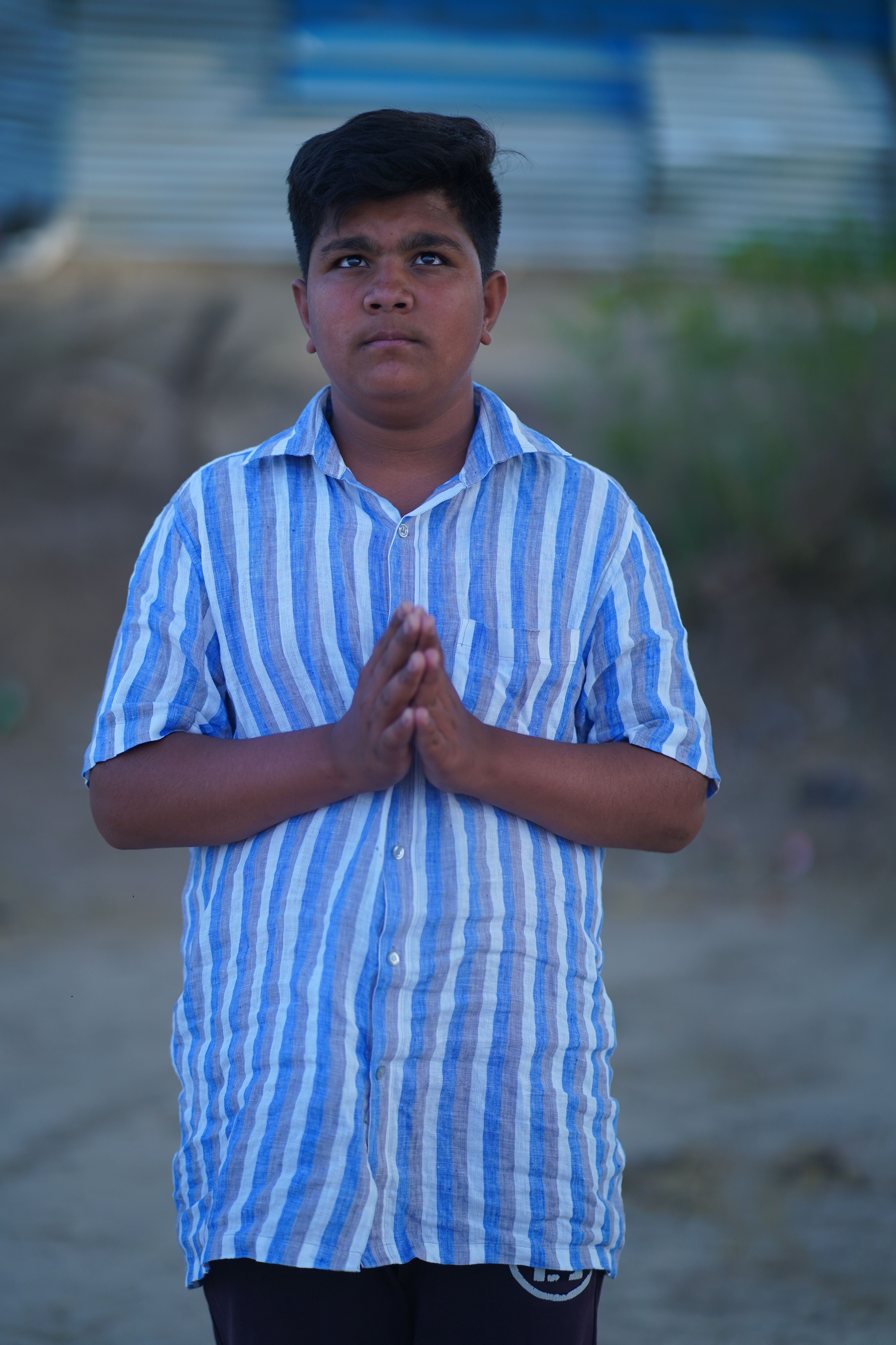 A serious teenager stands outdoors, hands folded, exuding spirituality and focus in prayer.