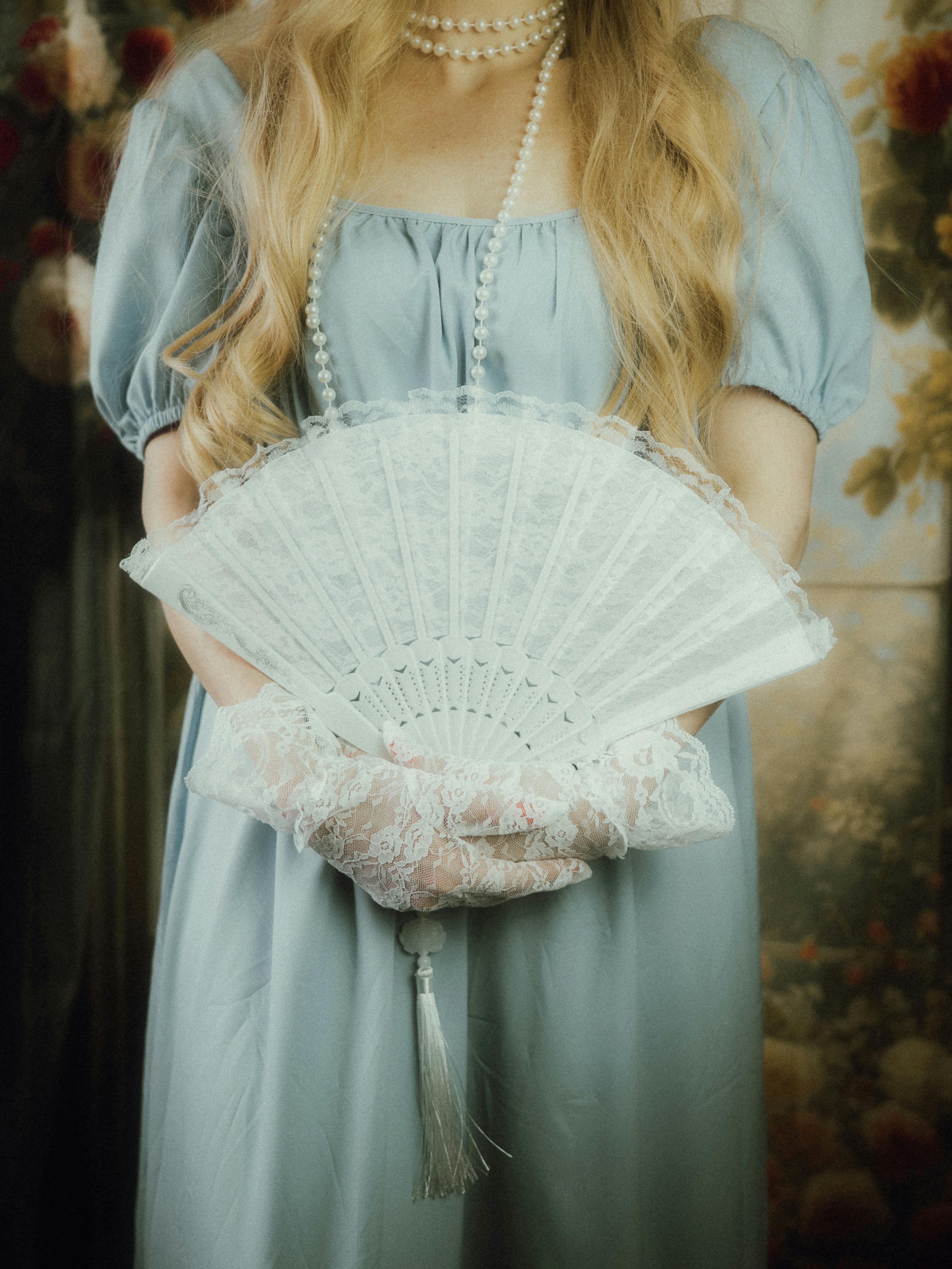 Elegant vintage portrait of woman in blue dress holding lace fan, pearls.