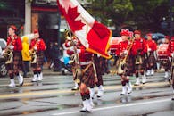 游行乐队身穿苏格兰短裙，冒雨在城市街道上举着加拿大国旗游行