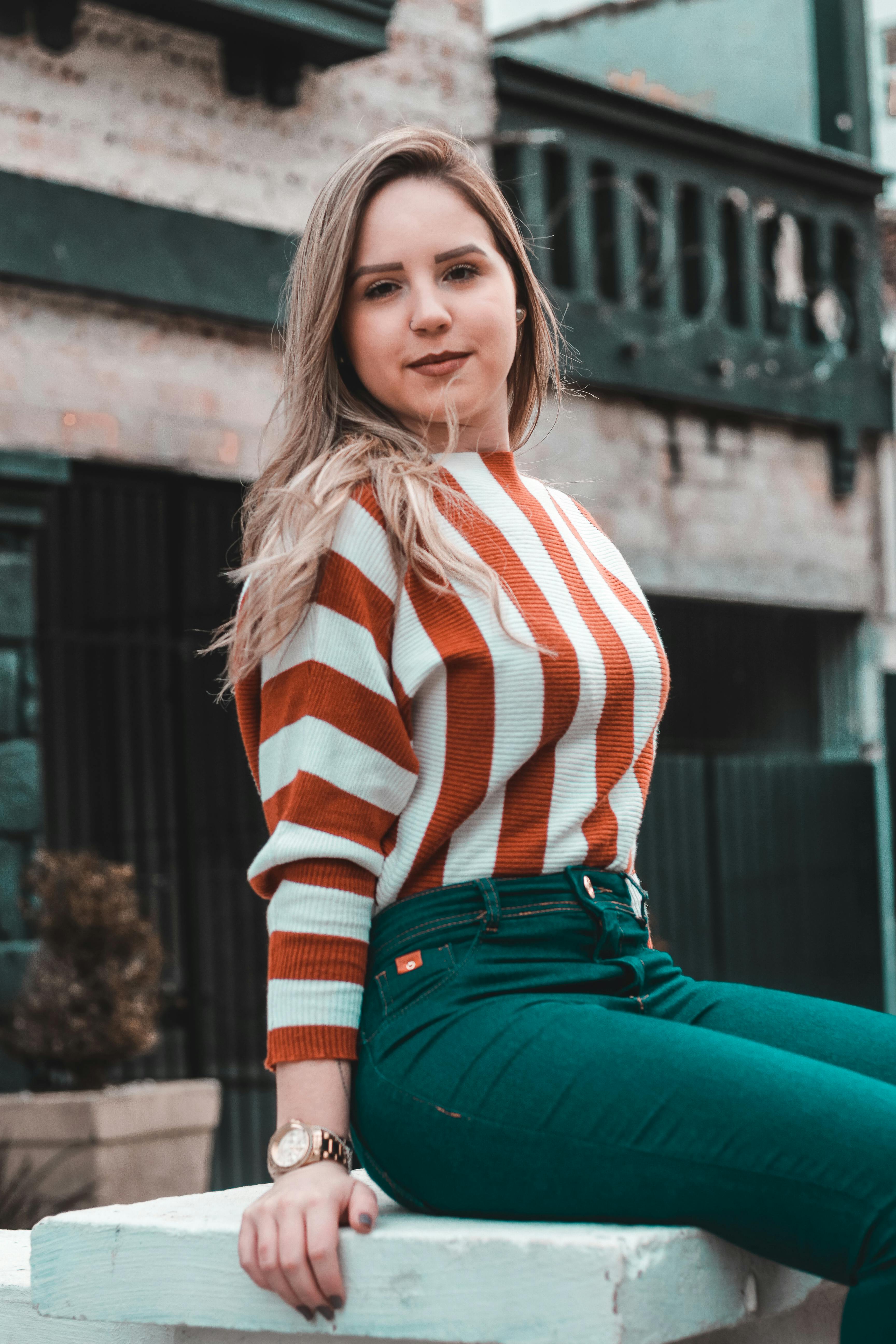 一位金发时尚女郎自信地坐在户外的条纹毛衣中