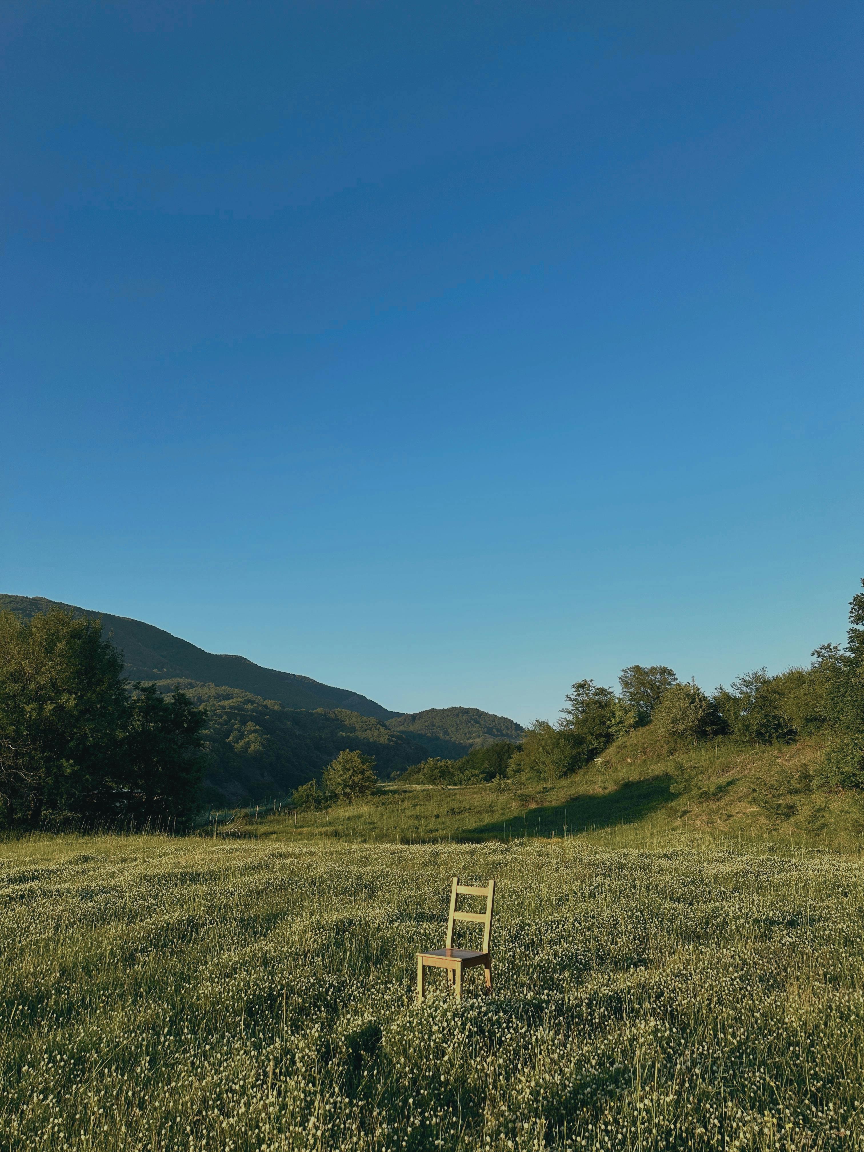 A solitary chair stands in a lush green meadow beneath a clear blue sky, evoking tranquility.