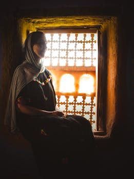 Silhouette of a woman with headscarf sitting by an ornate backlit window in Agdz, Morocco.