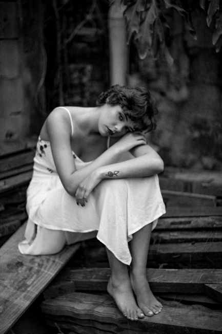 Monochrome portrait of a woman with short hair sitting outdoors, evoking emotion.