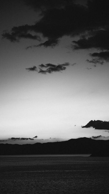 Monochrome coastal scene capturing silhouetted hills against the cloudy evening sky.