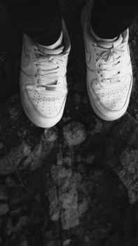 Close-up of white sneakers standing on rough rocks in black and white.