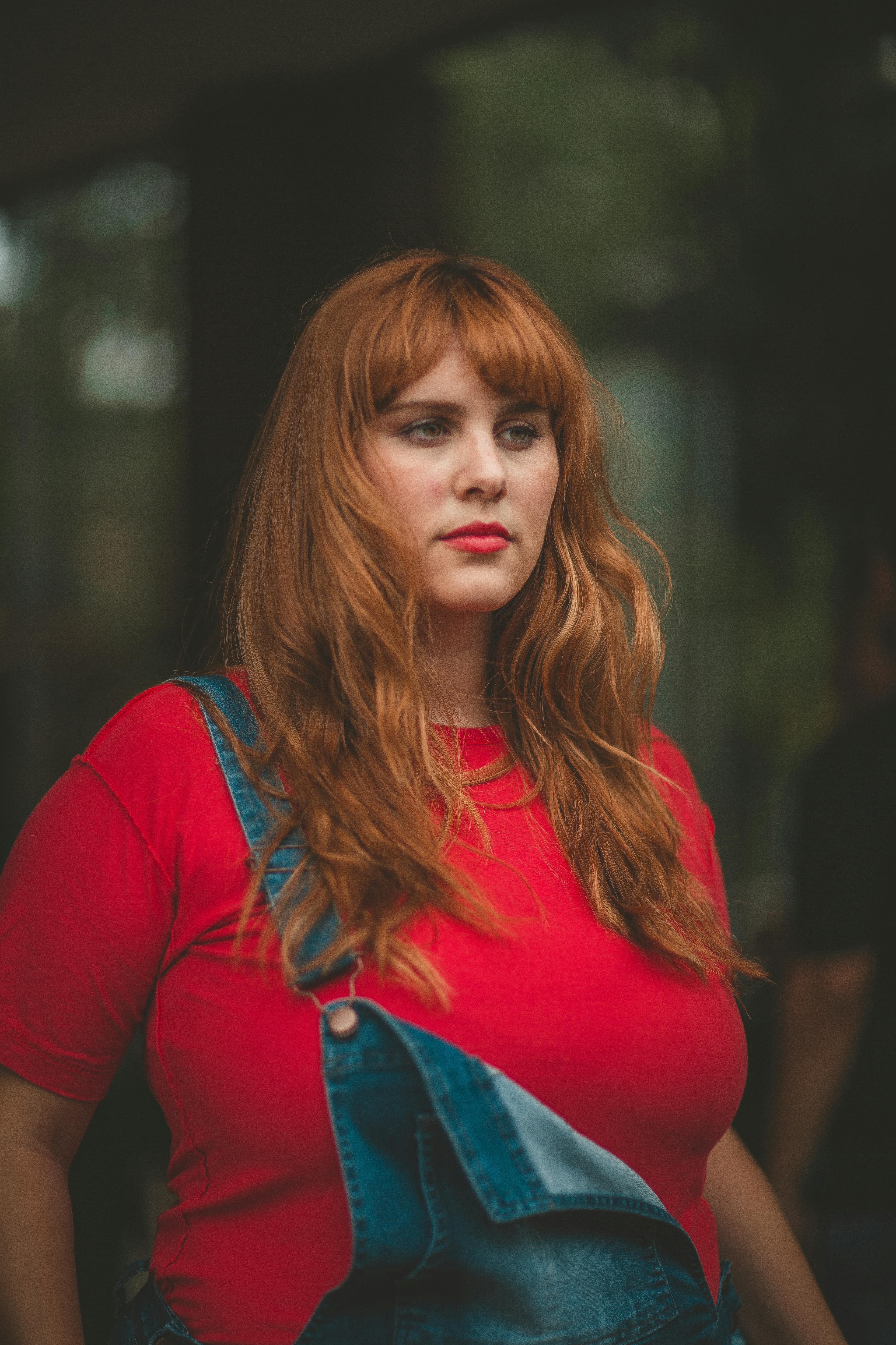 一位红发女子身着休闲装，在户外自信而体贴地摆着姿势