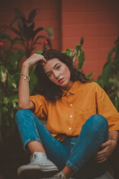 一位穿着黄色衬衫和牛仔裤的女人在植物前摆姿势