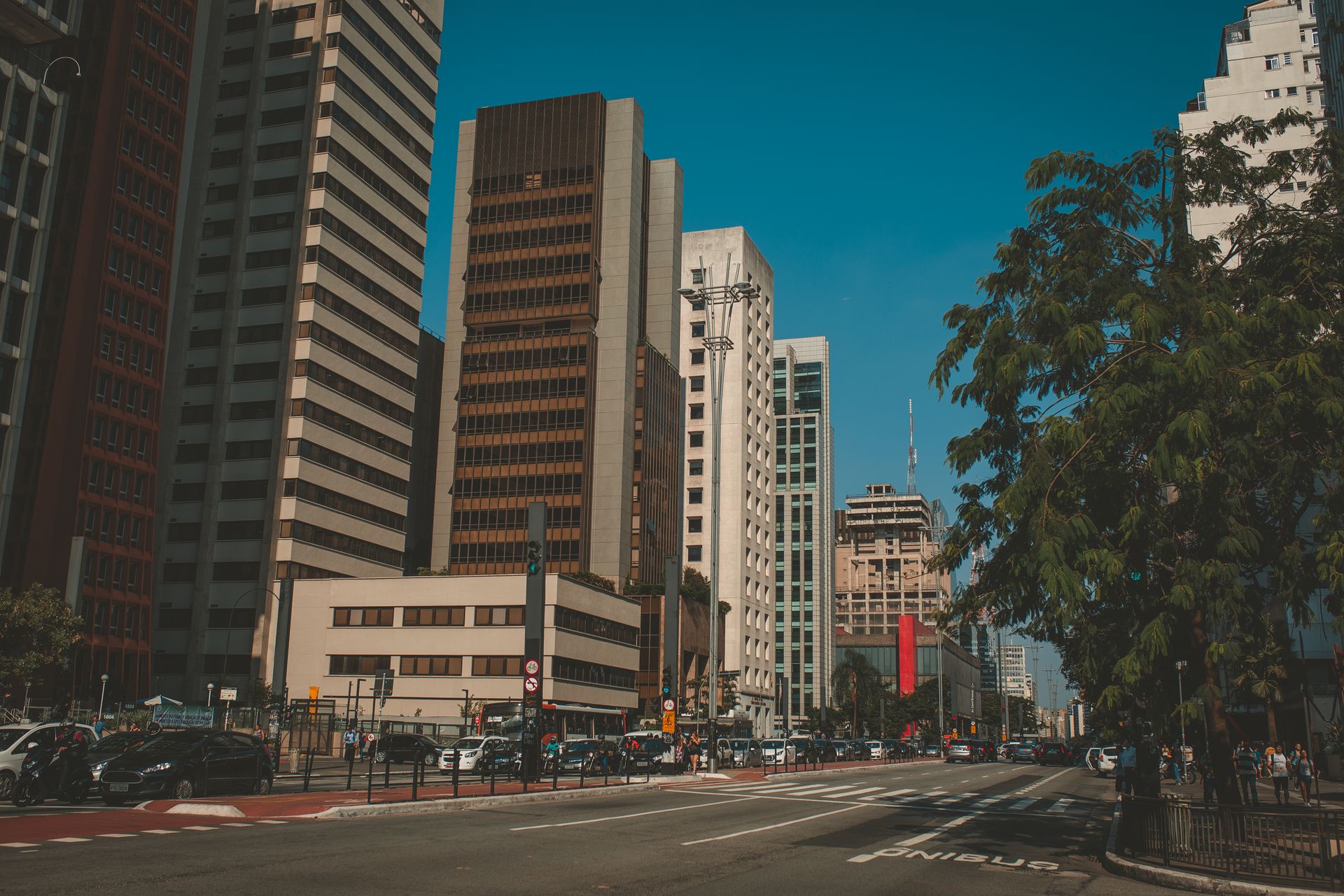 A bustling city street with modern skyscrapers, vehicles, and a clear blue sky.