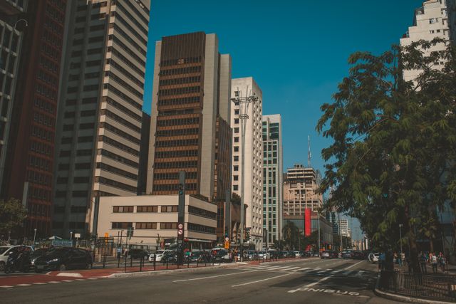 A bustling city street with modern skyscrapers, vehicles, and a clear blue sky.