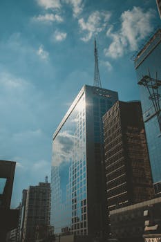 一座摩天大楼矗立在繁华的城市中，映照着云层和蓝天