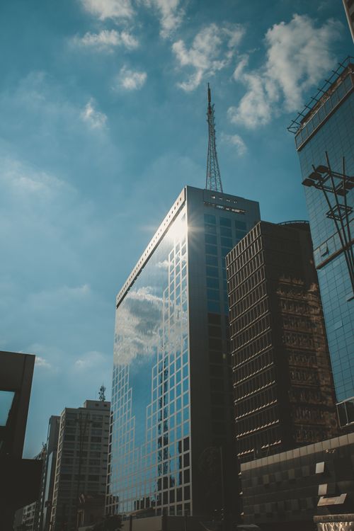 Free A sleek urban skyscraper reflecting clouds and blue sky in a bustling cityscape. Stock Photo