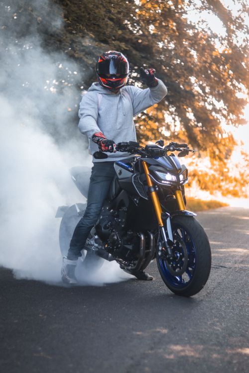 Free Man riding motorcycle performs a smoke burnout on sunny street, showcasing skill and style. Stock Photo