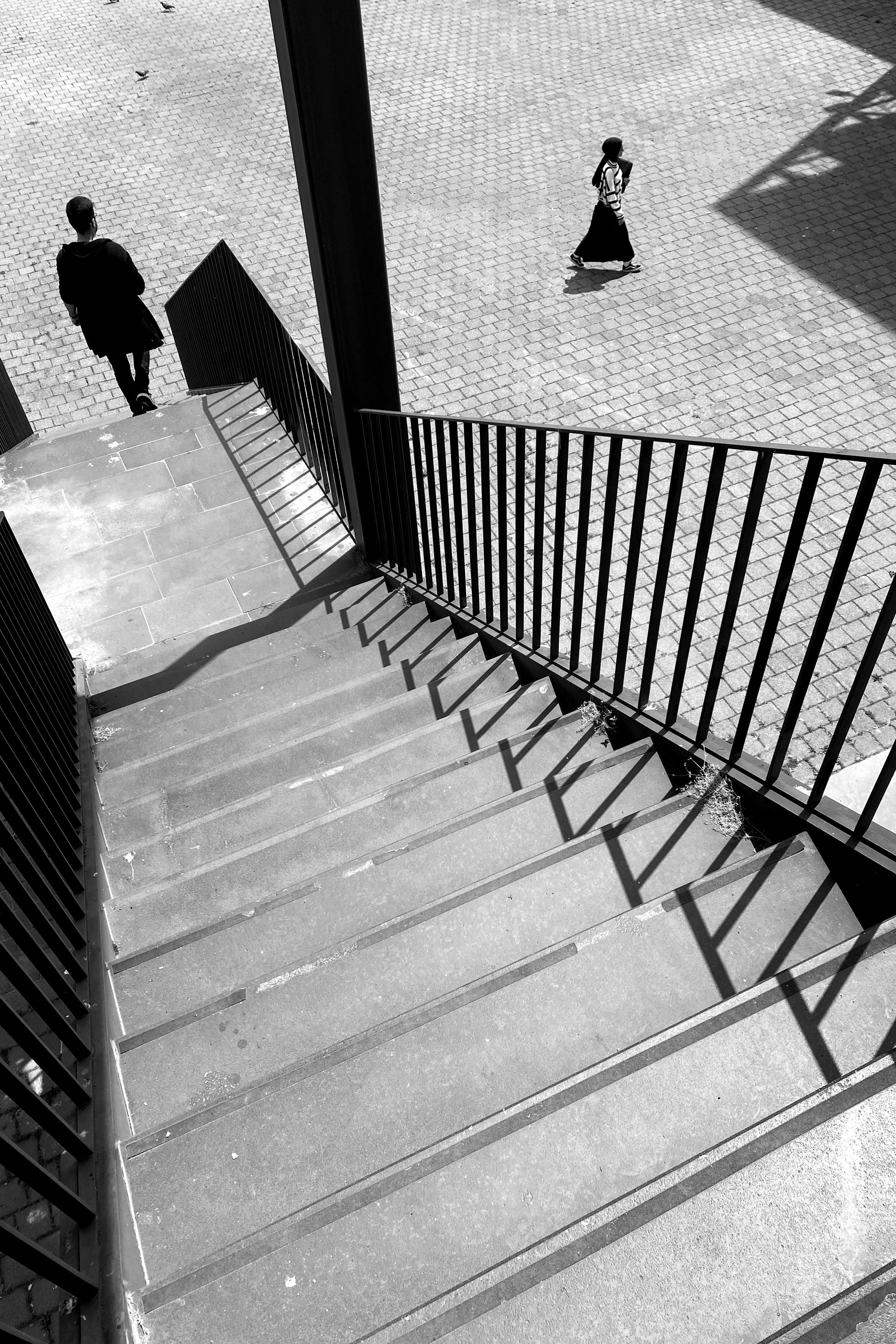 Black and white photo of two people walking near a staircase in an urban setting.