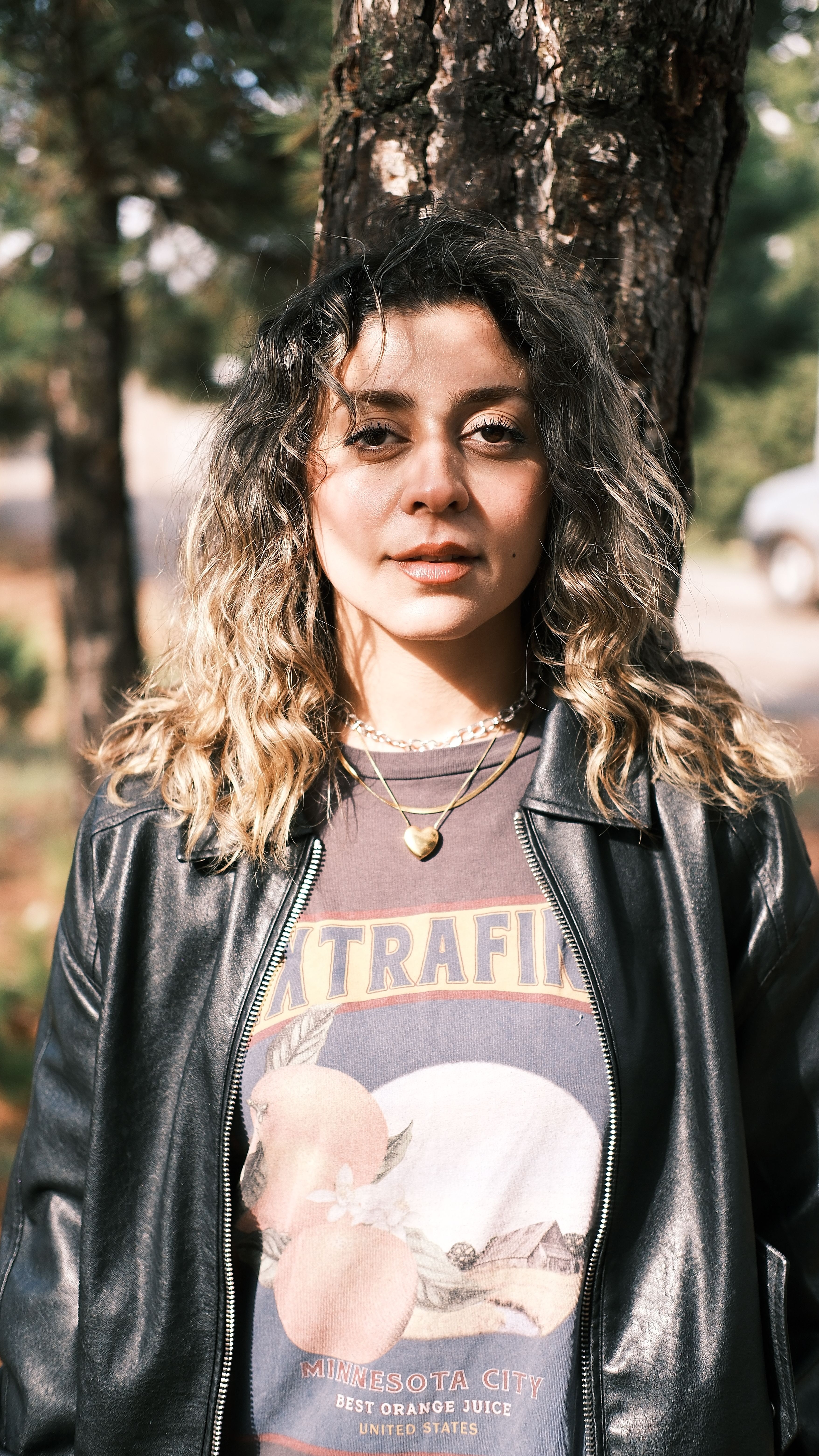 Fashionable young woman with curly hair posing outdoors in a leather jacket.