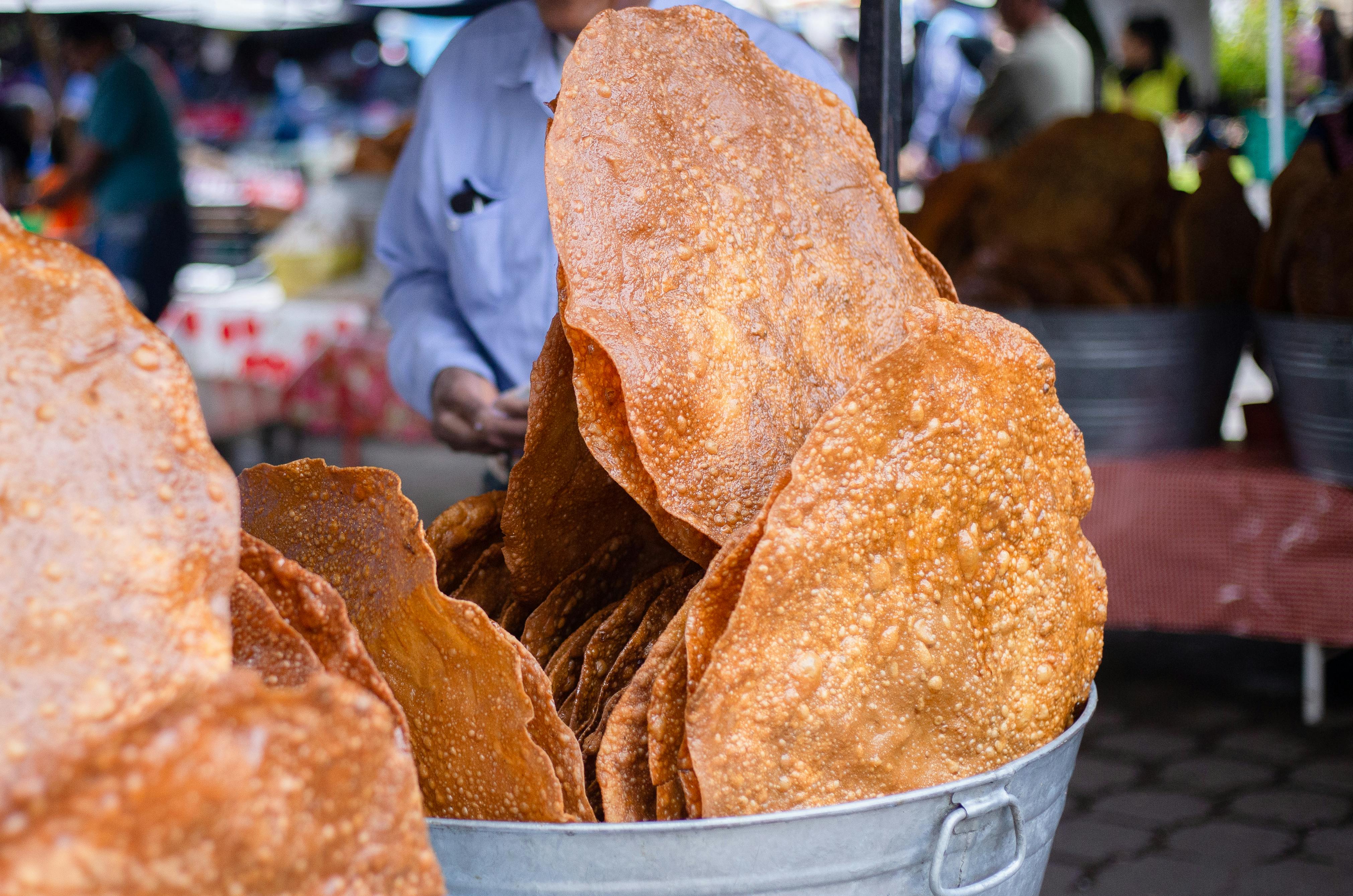 Close-up of crispy round flatbreads displayed in a metal bucket at a bustling outdoor market.
