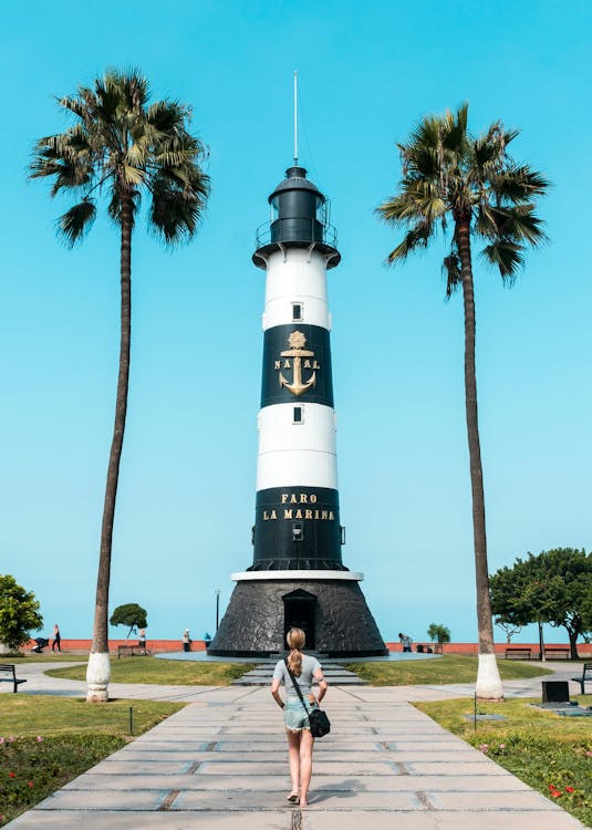 A woman walking towards a lighthouse with palm trees